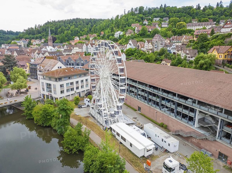 A Ferris wheel next to urban buildings embedded in a summer landscape with wooded hills, Ferris wheel construction, Calw, Black Forest, Germany