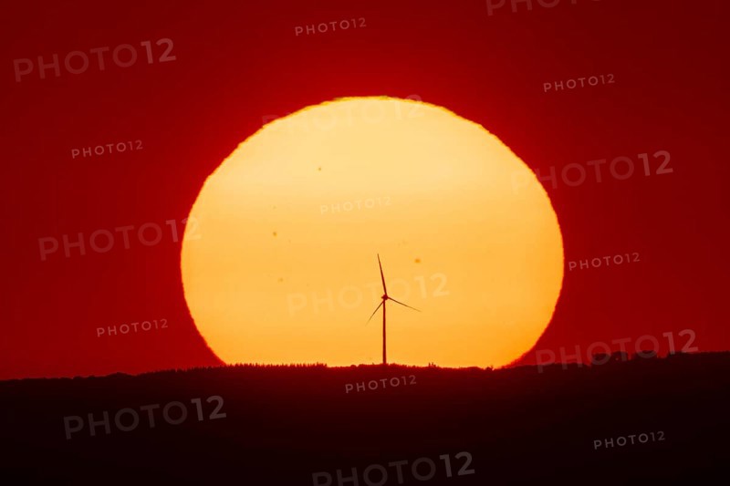 From the summit plateau of the Großer Feldberg in the Taunus mountains, you can watch the sun set behind a wind turbine on the distant horizon, Hesse, Germany