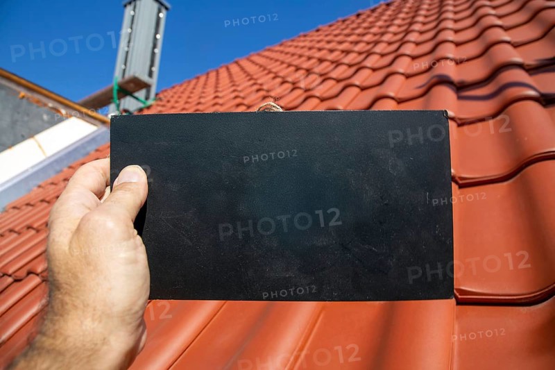 Man holding a sign with space for text in front of a recently tiled roof