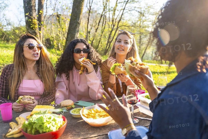 Group of friends having fun eating and drinking outdoors on a sunny day, celebrating friendship and good times together