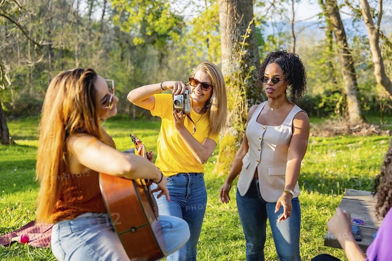 Group of friends soaking up the sun in nature, playing music, capturing moments with cameras, and enjoying each other's company