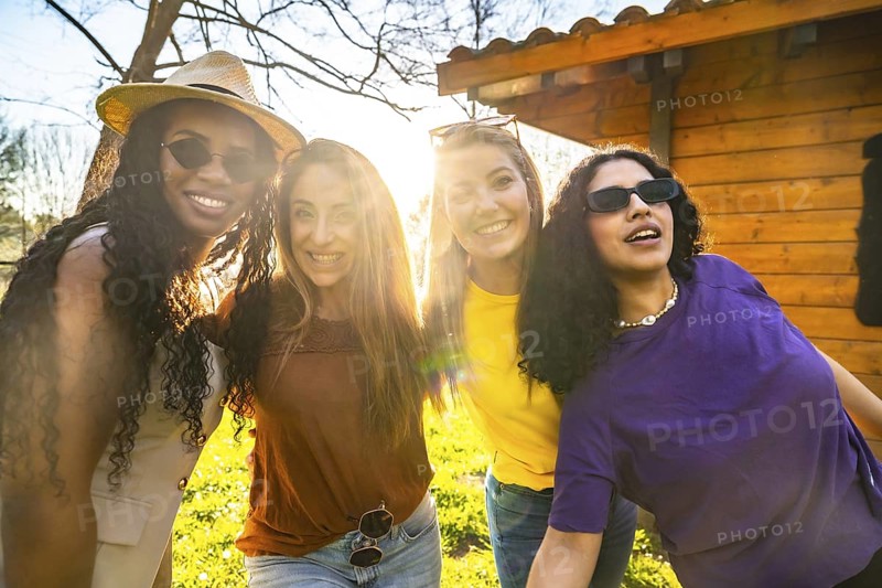 Four diverse young women are smiling and embracing outdoors, enjoying the warm glow of sunset light and celebrating their friendship