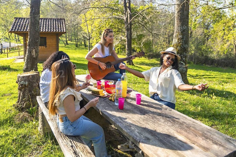 Four young women enjoying a sunny day at the park, playing music, eating fruit, and having fun together
