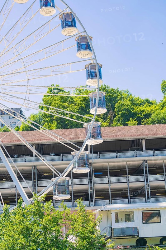 A large Ferris wheel towers over a building, surrounded by green trees under a clear blue sky, 950 years Calw, Germany