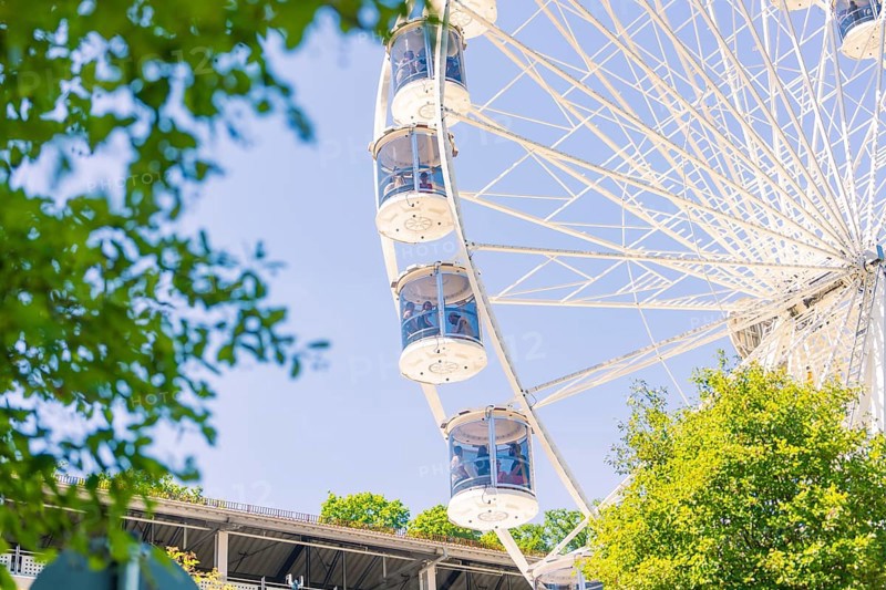 Close-up of a Ferris wheel with cabins, visible between green trees and a blue sky, 950 years Calw, Germany