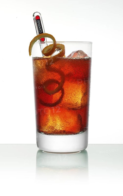Campari cocktail in a long drink glass on ice with orange zest as garnish against a white background, studio shot