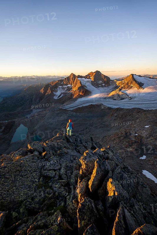 Mountaineer in front of picturesque high mountain landscape at sunrise with alpenglow, glacier and rocky mountain peaks in the morning light, view at the cup on mountain peak Königshofspitz and glacier Übeltalferner, Stubai Alps, South Tyrol, Italy