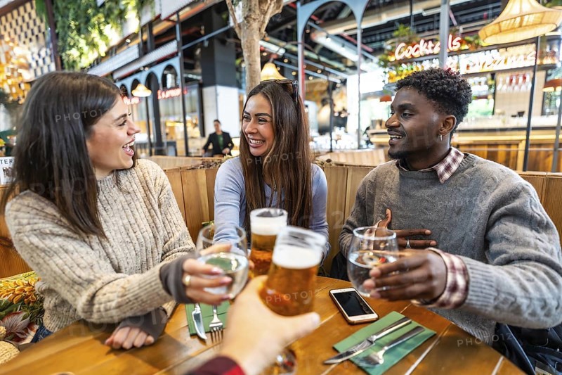 Group of cheerful multi ethnic friends toasting with beer and water at brewery pub restaurant, enjoying time together