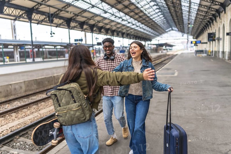 Happy multi ethnic friends meeting at train station, hugging each other, and starting their vacation together