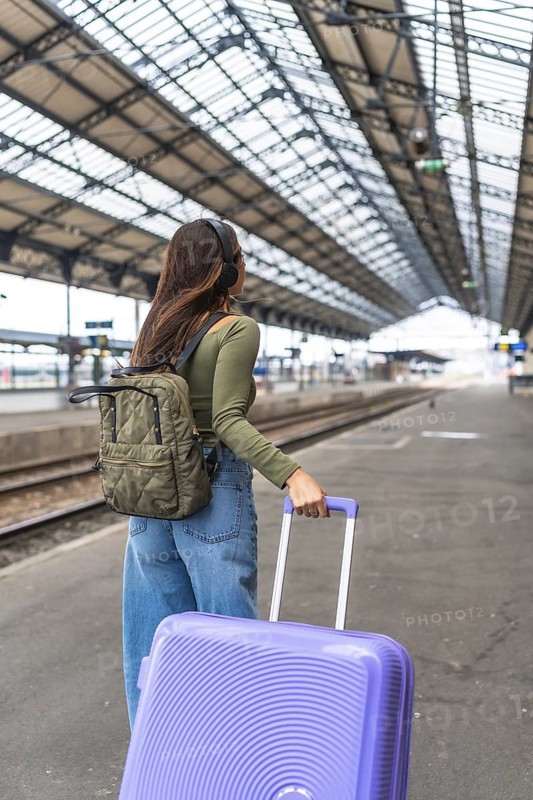 Tourist wearing headphones and carrying luggage strolls through a bustling train station, embracing the excitement of travel and adventure