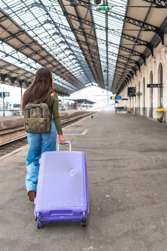 Tourist walking along a train platform, pulling a trolley suitcase while embarking on an exciting travel adventure
