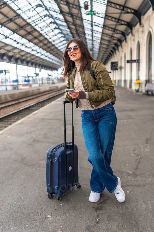 Tourist using a smartphone while waiting for the train at the railway station, enjoying the journey and planning the next destination
