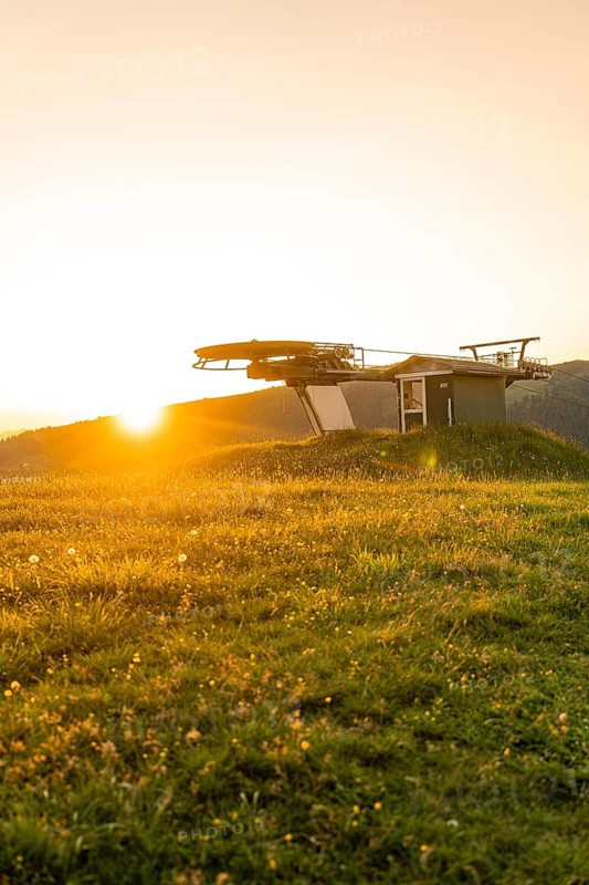 Sunset over a green meadow with a silhouette of a cable car station, Alpe di Siusi, Dolomites, South Tyrol, Italy