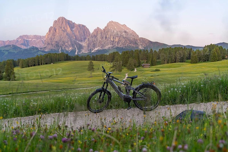 A bicycle stands on a gravel road with a view of the nearby Dolomites, Sassolungo Group, Alpe di Siusi, Dolomites, South Tyrol, Italy