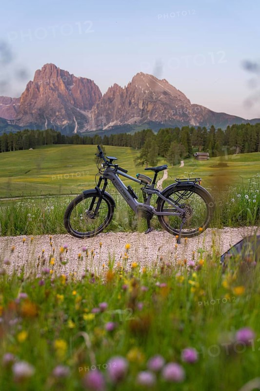 E-bike on a gravel road in front of the imposing silhouette of the Dolomites in the evening light, Alpe di Siusi, Sassolungo Group, Dolomites, South Tyrol, Italy