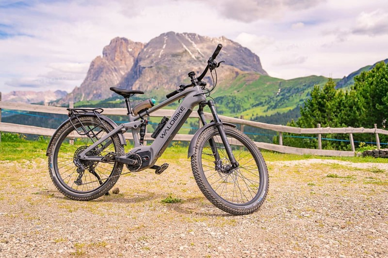 Grey e-bike on a stony path with mountain view and wooden fence in the background, Alpe di Siusi, Dolomites, South Tyrol, Italy