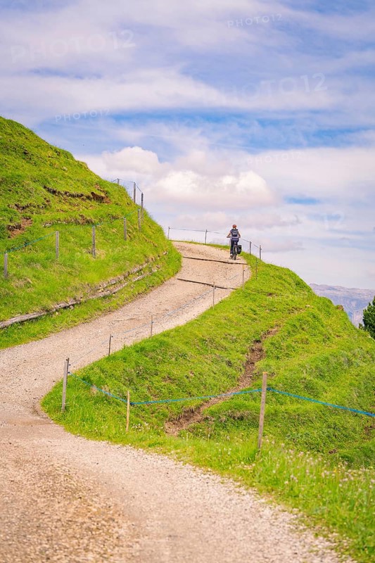Motorcyclist on a winding gravel road in a hilly landscape, Alpe di Siusi, Dolomites, South Tyrol, Italy