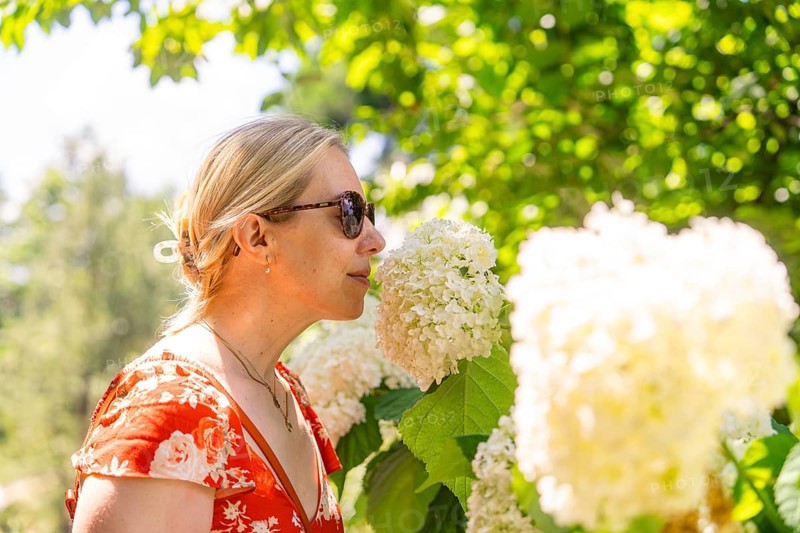 Woman in a red dress smelling a white flower, surrounded by green plants, Botanical Garden, The Gardens of Trauttmansdorff Castle, Merano, South Tyrol, Italy