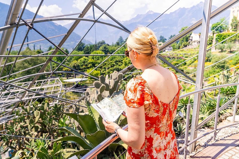 Woman in a red summer dress looking at a map in front of a glass construction, Botanical Garden, The Gardens of Trauttmansdorff Castle, Merano, South Tyrol, Italy
