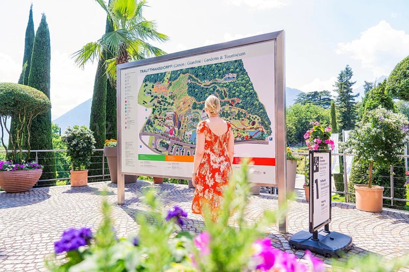 Woman in front of an information board in a sunny garden area, Botanical Garden, The Gardens of Trauttmansdorff Castle, Merano, South Tyrol, Italy