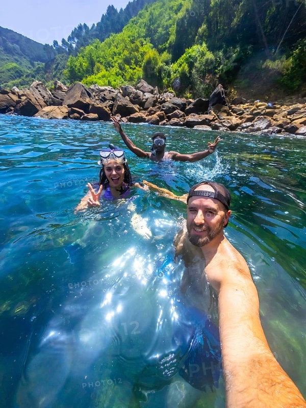 Three friends enjoy snorkeling in the refreshing ocean water, capturing a selfie moment amidst a beautiful coastal landscape