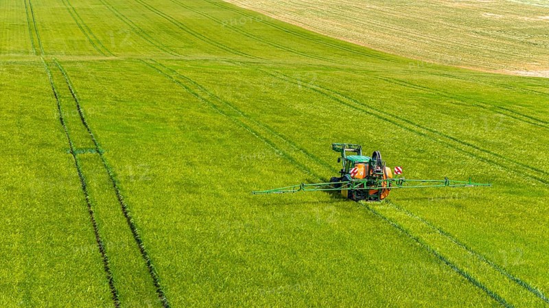 Farmer with tractor working in the field. In early summer, he fertilises the grain for an optimum yield. Drone photo. Merklingen, Baden-Württemberg, Germany