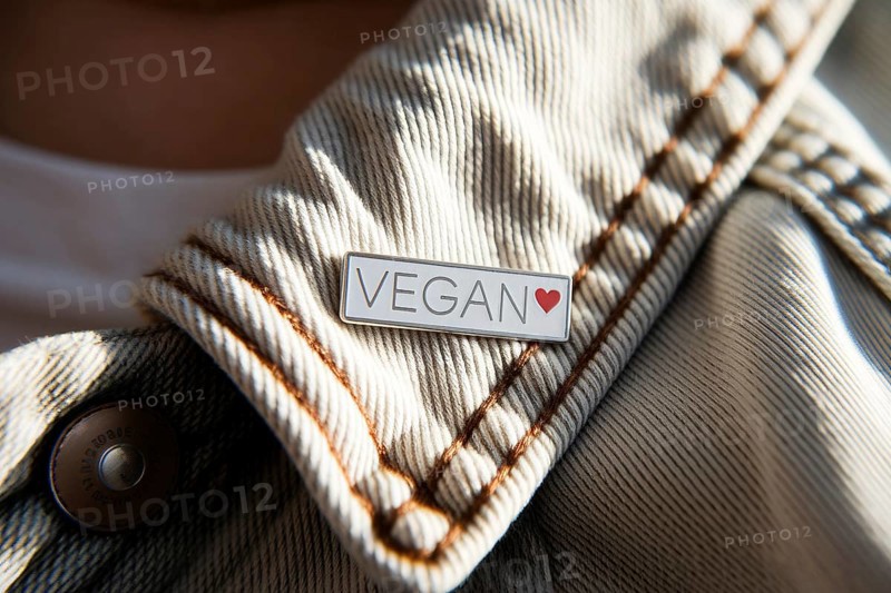 Close-up of silver pin with VEGAN text and red heart on worn cotton jacket. Symbol of ethical lifestyle and compassionate choice. Generative ai, AI generated