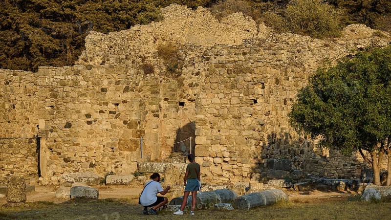 Two people in front of an old stone wall in a setting surrounded by trees, Roman bathhouse, Asklipion, Asklepieion, healing temple, temple, Hippocrates, Kos, Dodecanese, Greek Islands, Greece