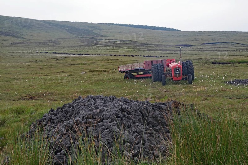 Old red tractor standing in boggy fields against a hilly backdrop with grey sky, peat cutting, Isle of Harris, Hebrides, Scotland, United Kingdom
