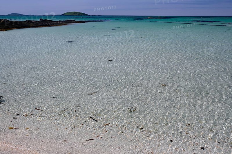 Crystal clear turquoise water on a sandy beach with islands on the horizon under a blue sky, Eriksay, Hebrides, Scotland, United Kingdom