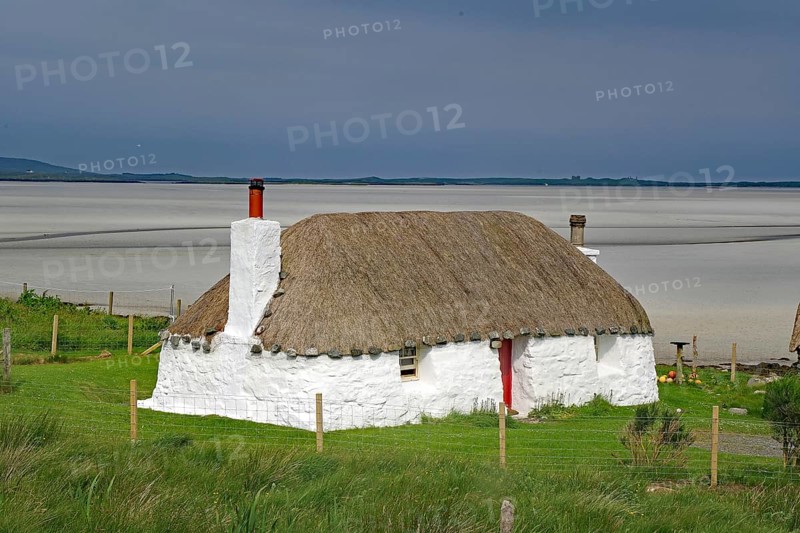 White thatched house on a green meadow against a sandy coastal background under a blue sky, holiday, holiday home, North Uist, Hebrides, Scotland, Great Britain