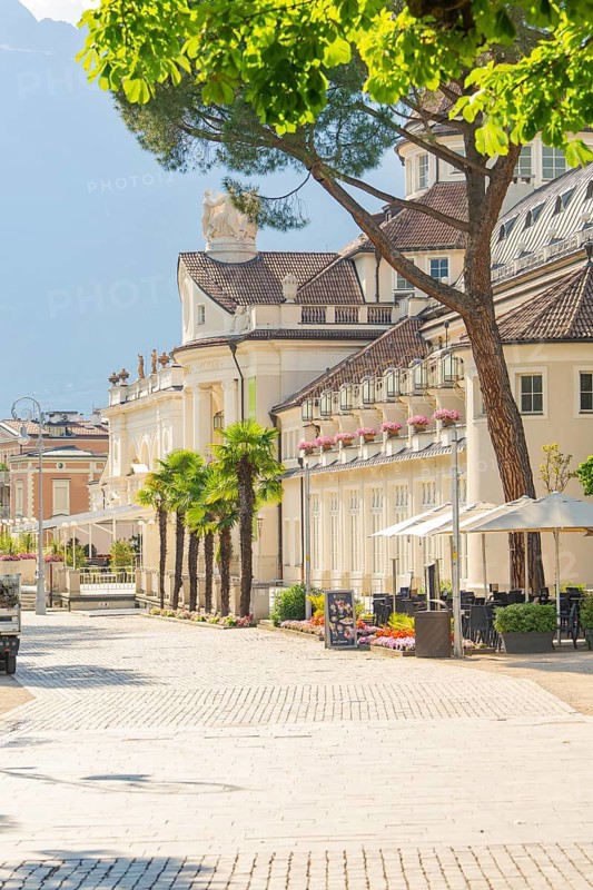Picturesque street lined with palm trees and inviting café, classic buildings in the background, Merano, Italy
