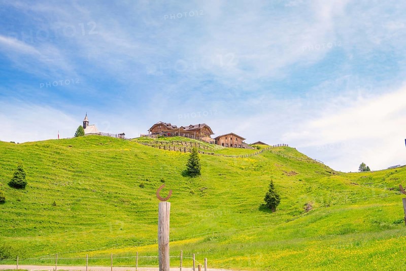 Wooden building on a green hill in front of a blue sky with white clouds, Alpe di Siusi, Dolomites, South Tyrol, Italy