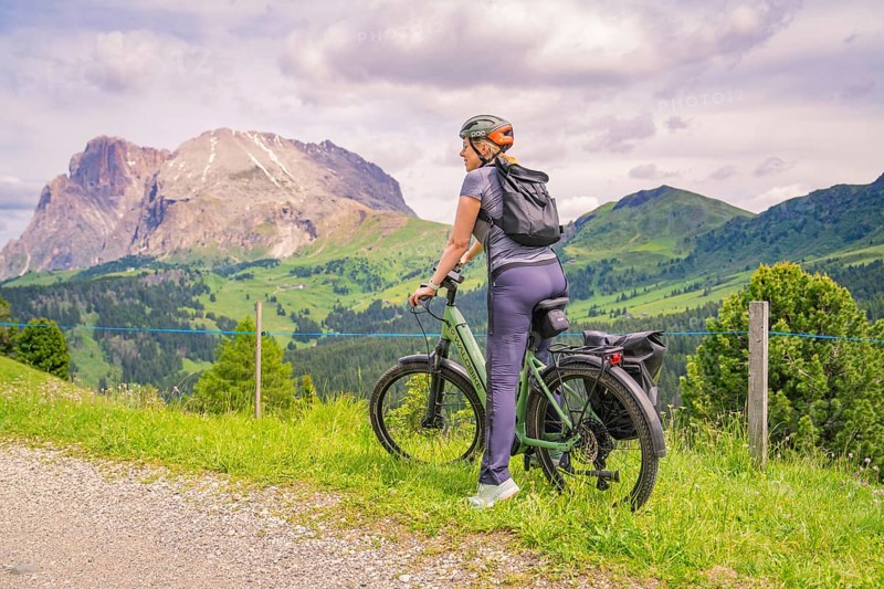 Cyclist on a path with a view of a mountain landscape under a cloudy sky, Alpe di Siusi, Dolomites, South Tyrol, Italy