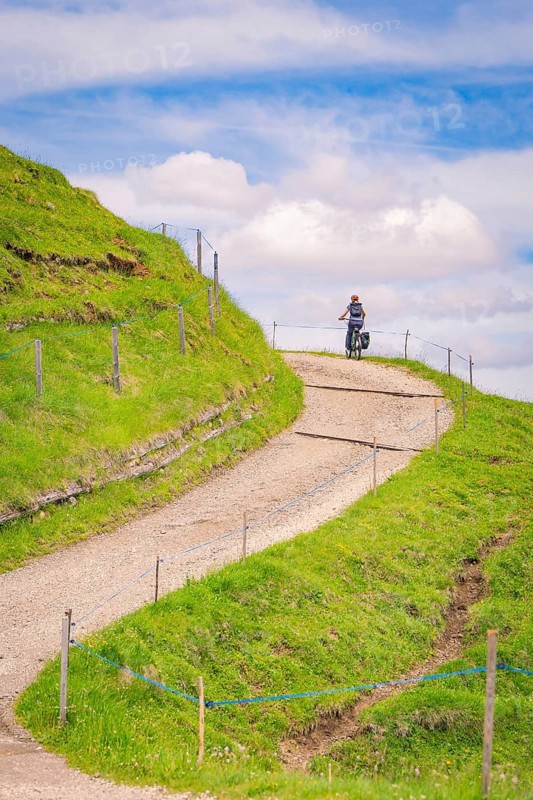 A cyclist rides on a winding hilly path in sunny weather, Alpe di Siusi, Dolomites, South Tyrol, Italy