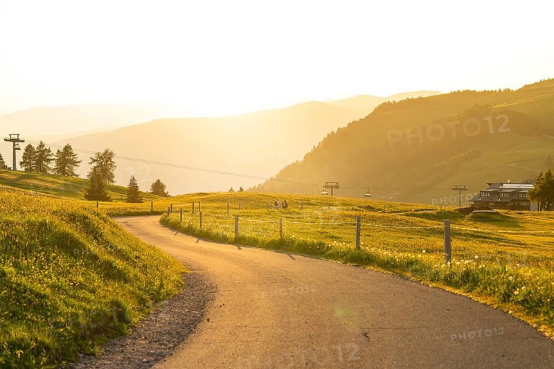 Curved road through a hilly landscape with cable cars at sunset, Alpe di Siusi, Dolomites, South Tyrol, Italy