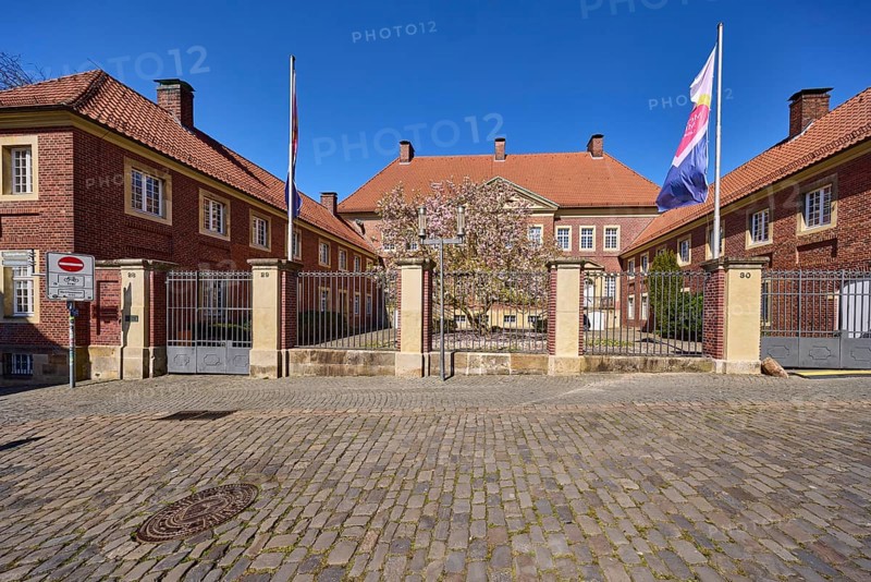 Cathedral administration, brick building, tree, cobblestone pavement, flags on flagpoles, blue cloudless sky, cathedral square, Münster, Münsterland, independent city, North Rhine-Westphalia, Germany