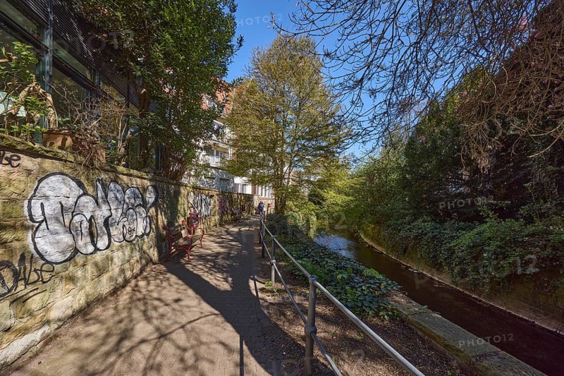 Footpath, sandstone wall, graffiti, metal railing, river Münstersche Aa, trees, bushes, shadow, blue cloudless sky, Schwester-Laudeberta-Weg, Münster, Münsterland, independent city, North Rhine-Westphalia, Germany