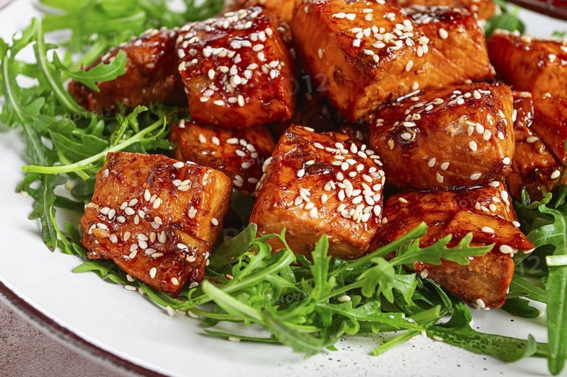 Fried salmon slices, teriyaki with sesame seeds, with arugula salad, top view