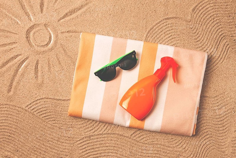 Drawing on the sand, sun and waves, sunglasses, with an orange bottle, beach towel, sun spray, on the sand, top view, no people