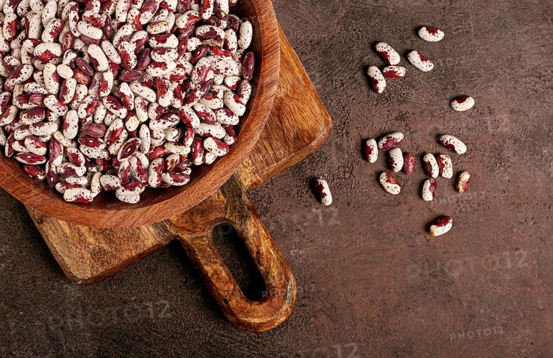 Variegated beans, red with white spots, raw in a wooden bowl, top view, no people