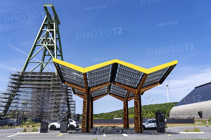 Electric filling station on the site of the former Lohberg colliery in Dinslaken, operated by Fastned, uses electricity from wind power and solar energy, fast-charging columns, with its own solar roof, in the background the 11, 500 square metre solar roof on the colliery's former coal mixing hall, wind farm on the Lohberg slagheap, Lohberg colliery headframe, North Rhine-Westphalia, Germany