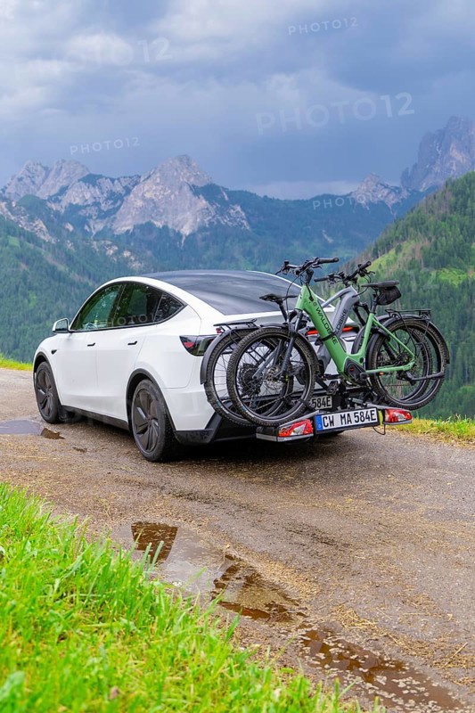 White car with bicycles on wet road, surrounded by mountains and rain clouds, electric car on holiday, Dolomites, South Tyrol, Dolomites, Italy