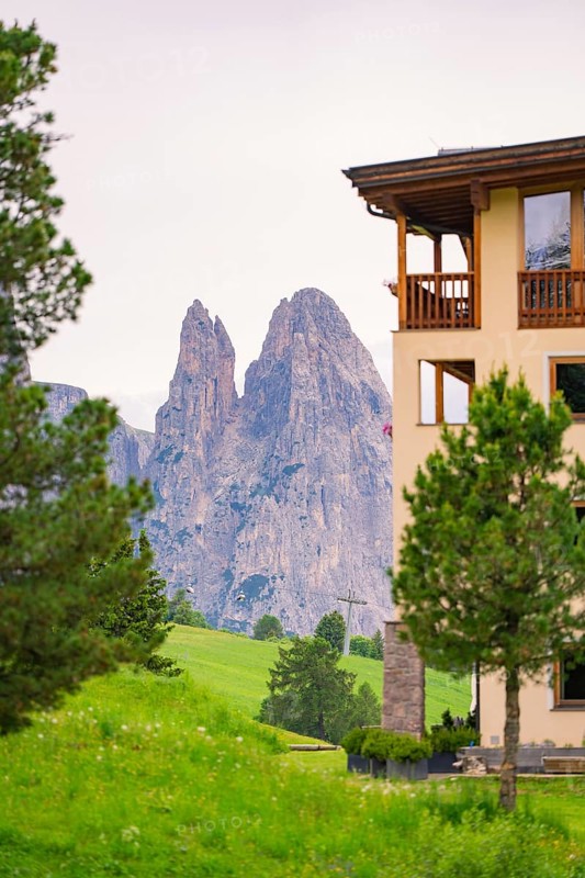 View of impressive rock formations behind a building with green foreground, Alpe di Siusi, South Tyrol, Dolomites, Italy