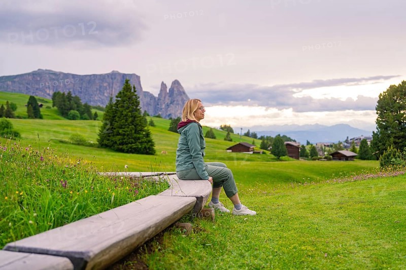 Woman enjoying the view in a green hilly landscape with mountains and clouds, Alpe di Siusi, South Tyrol, Dolomites, Italy