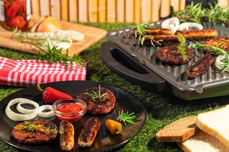 Burgers and sausages on a plate and grill with bread, rosemary and ketchup in a summery atmosphere
