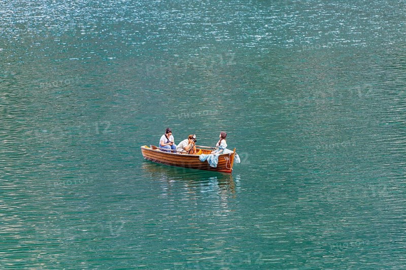 Three people in a small wooden boat on a quiet lake enjoying a relaxing trip, Lake Braies, South Tyrol, Dolomites, Italy