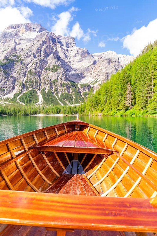 An empty wooden boat on a clear mountain lake with a view of steep rocks and wooded hills, Pragser Wildsee, South Tyrol, Dolomites, Italy