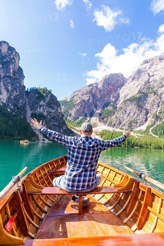 Man spreads his arms with joy on a boat on a mountain lake, Pragser Wildsee, South Tyrol, Dolomites, Italy