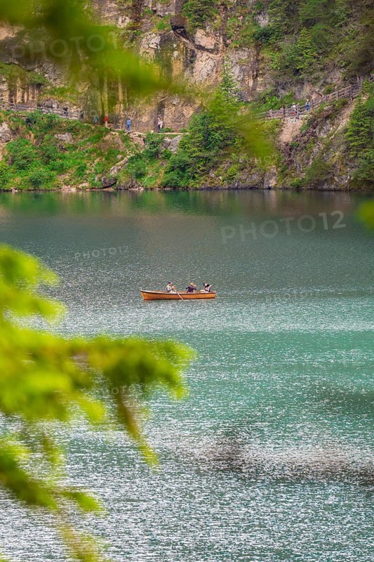 A small wooden boat with people on a quiet lake surrounded by trees, Pragser Wildsee, South Tyrol, Dolomites, Italy